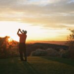 Golfer teeing off into the sunset on the golf course.