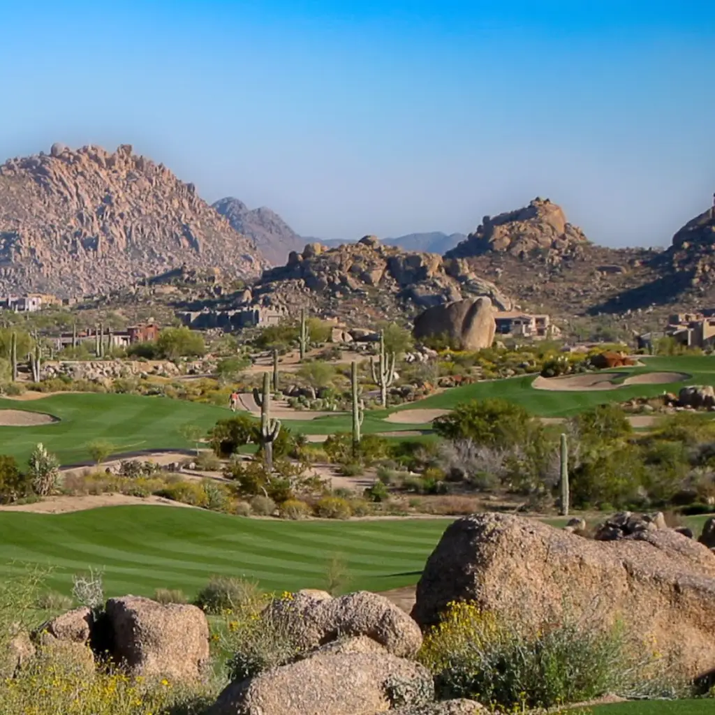 Golf fairway winding between boulders and rugged desert mountains.