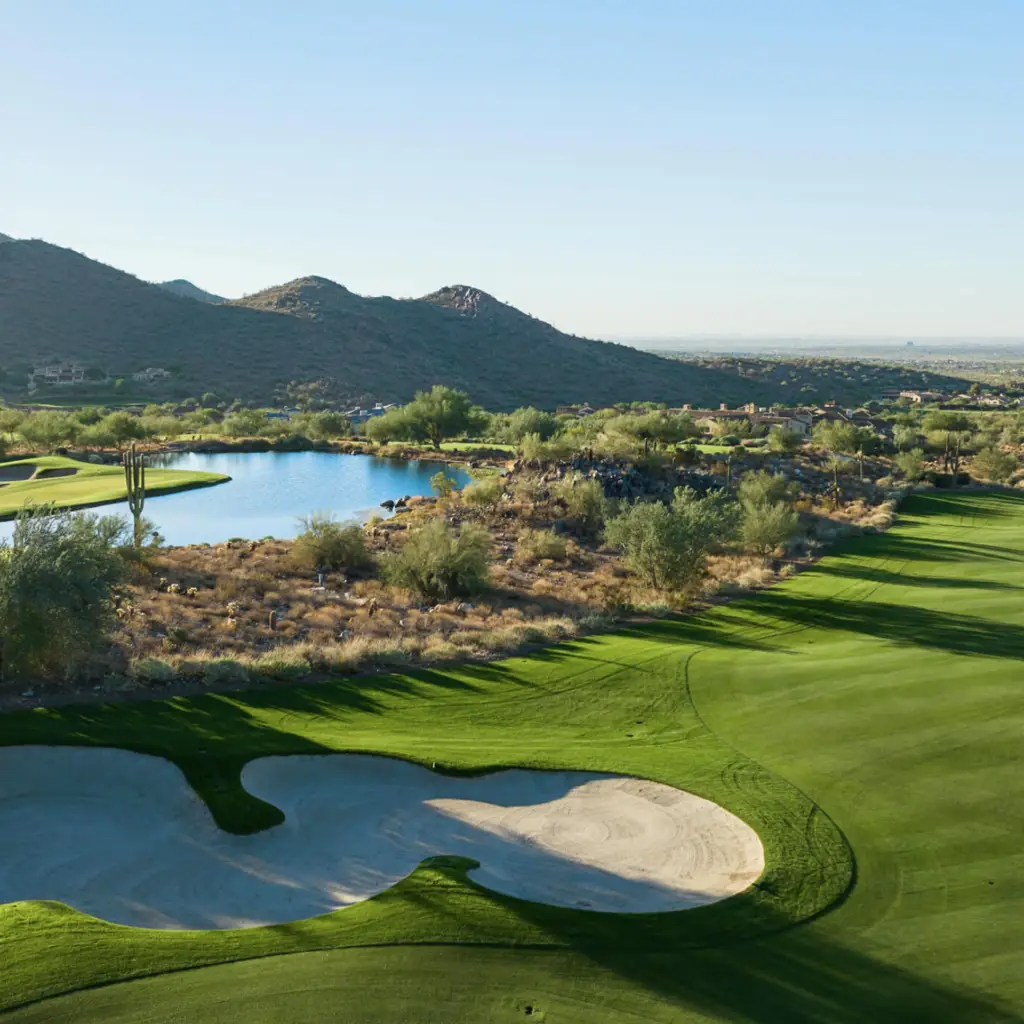 Golf greens, sand bunkers, and water framed by desert hills.