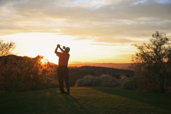 Golfer teeing off into the sunset on the golf course.
